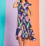 Woman wearing tropical abstract print midi wrap dress with flutter sleeves and asymmetrical hem