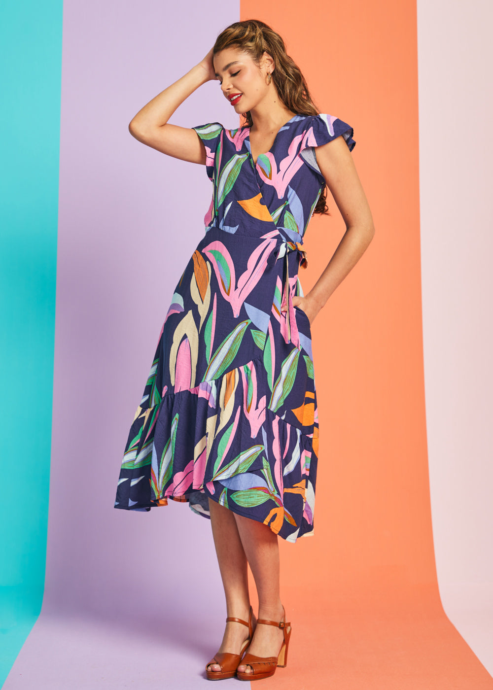 Woman posing in navy tropical print midi dress with flutter sleeves and asymmetrical hem