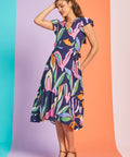 Woman posing in navy tropical print midi dress with flutter sleeves and asymmetrical hem
