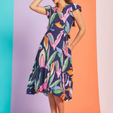 Woman posing in navy tropical print midi dress with flutter sleeves and asymmetrical hem