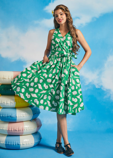 Model wearing green seashell print faux-wrap vacation dress with waist tie and flowy skirt
