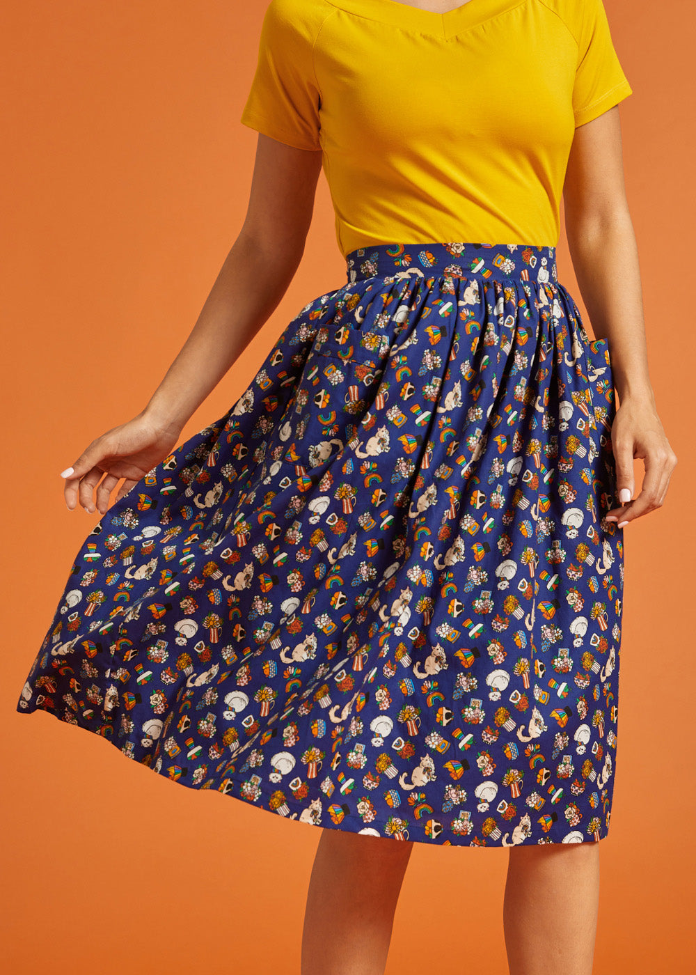 Woman wearing a yellow top and blue patterned skirt on an orange background