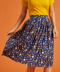 Woman wearing a yellow top and blue patterned skirt on an orange background