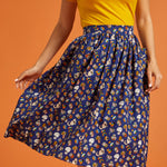 Woman wearing a yellow top and blue patterned skirt on an orange background