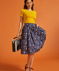 Woman in yellow top and novelty print skirt holding a vintage radio against an orange background
