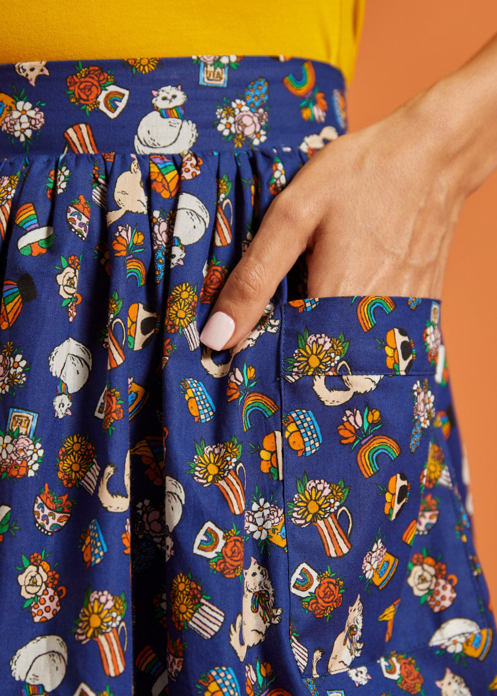 Close up of pocket on colorful patterned fabric skirt with cats and rainbows on a blue background