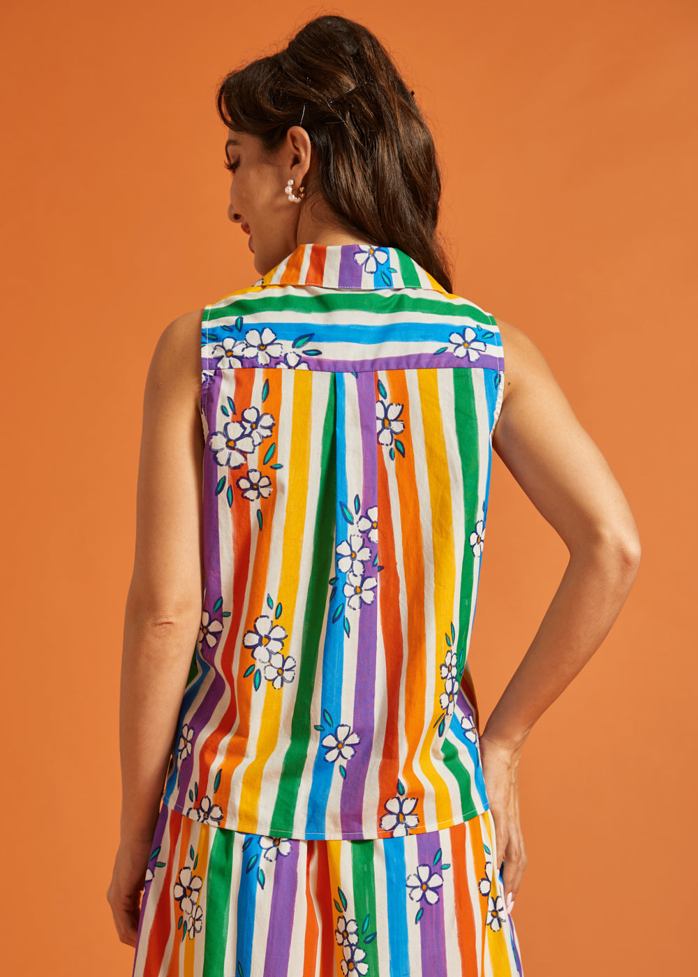 Back view of woman wearing a colorful striped shirt with floral patterns on an orange background