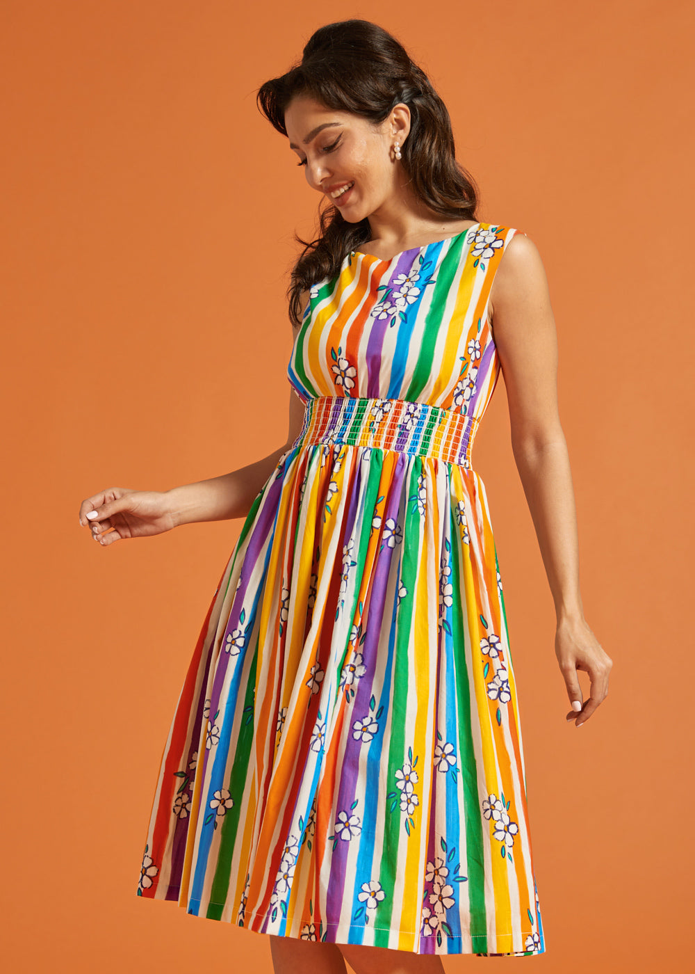 Woman wearing a rainbow stripe pride dress against an orange background