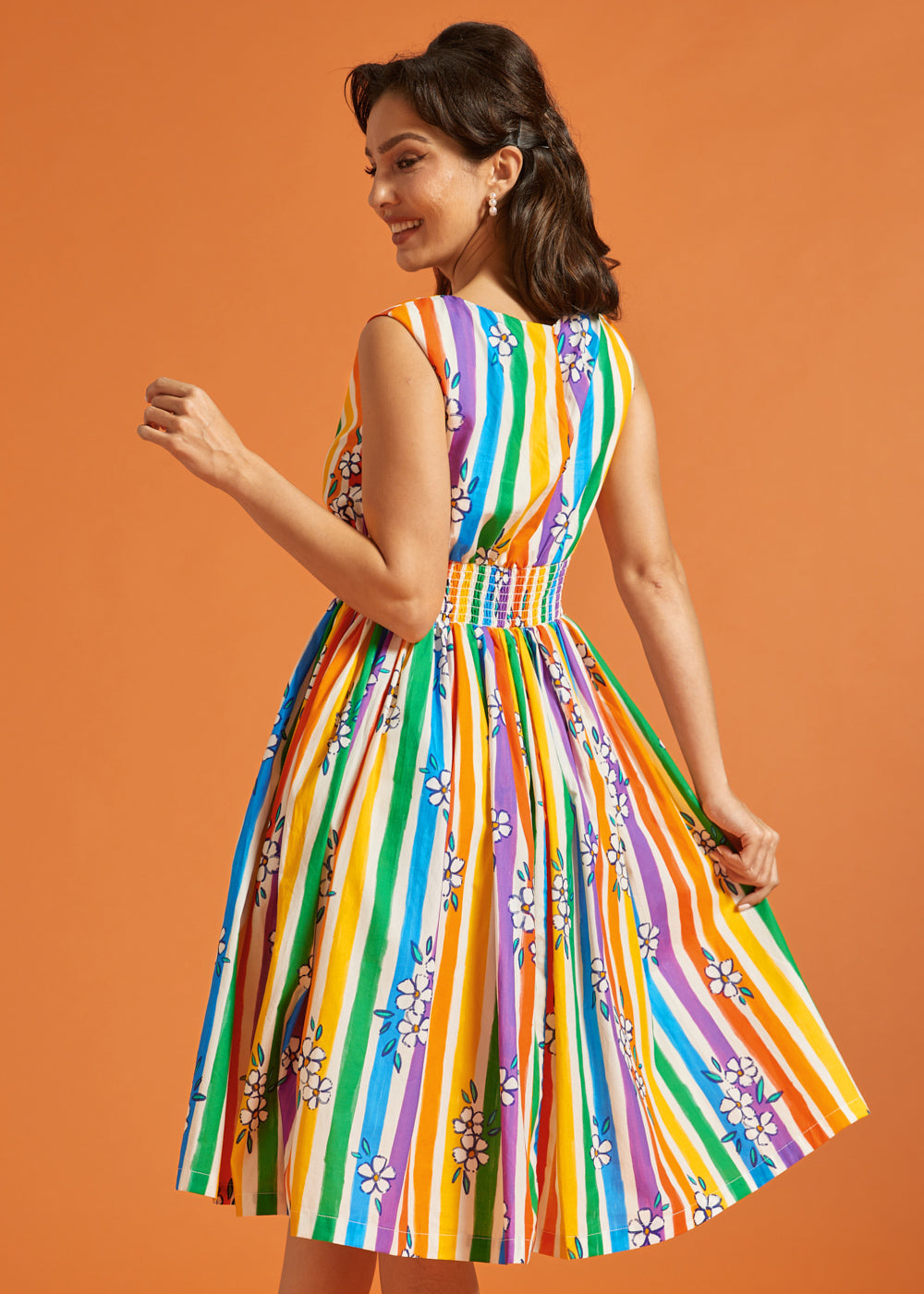 Woman wearing a colorful striped summer dress against an orange background