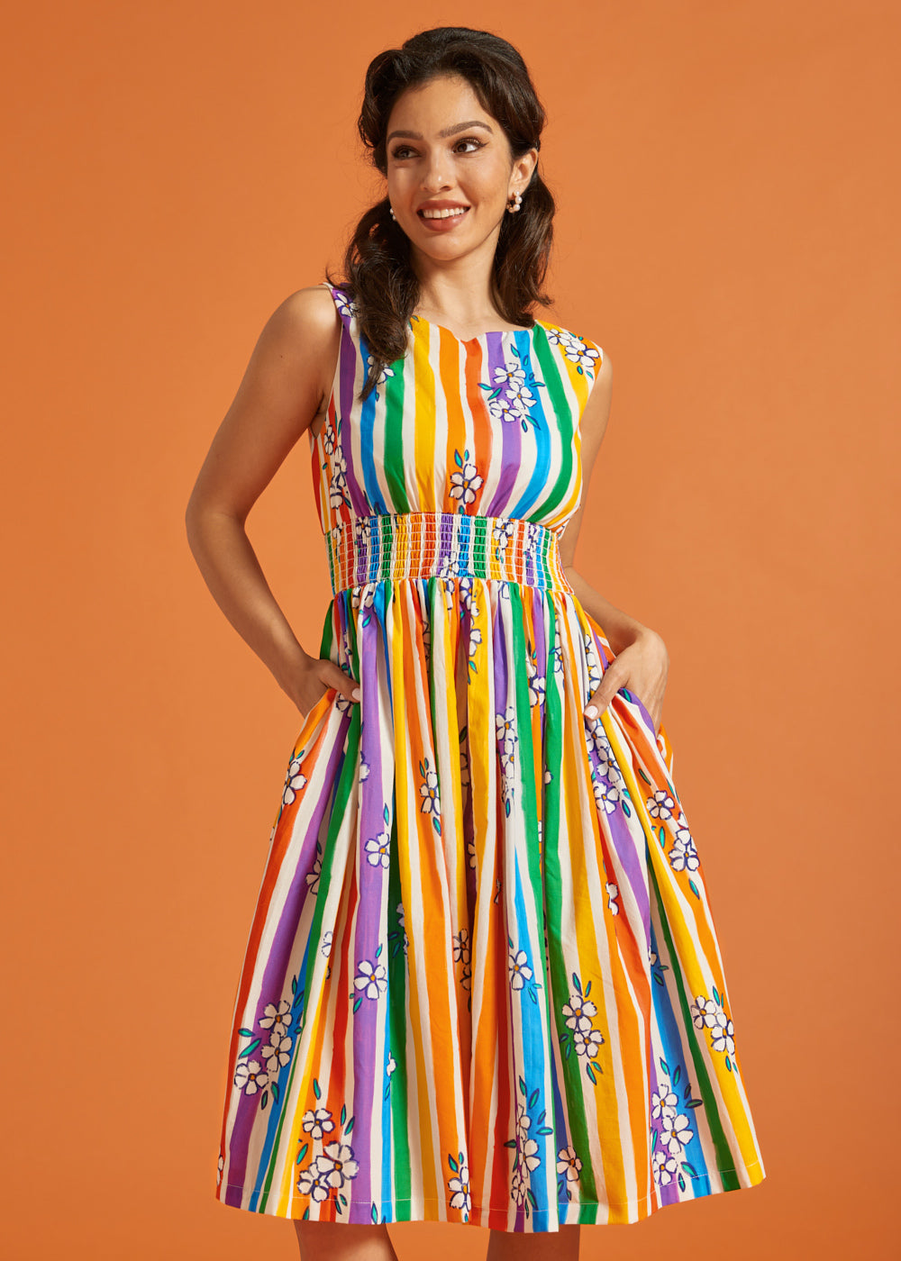 Woman wearing a colorful rainbow striped summer dress against an orange background