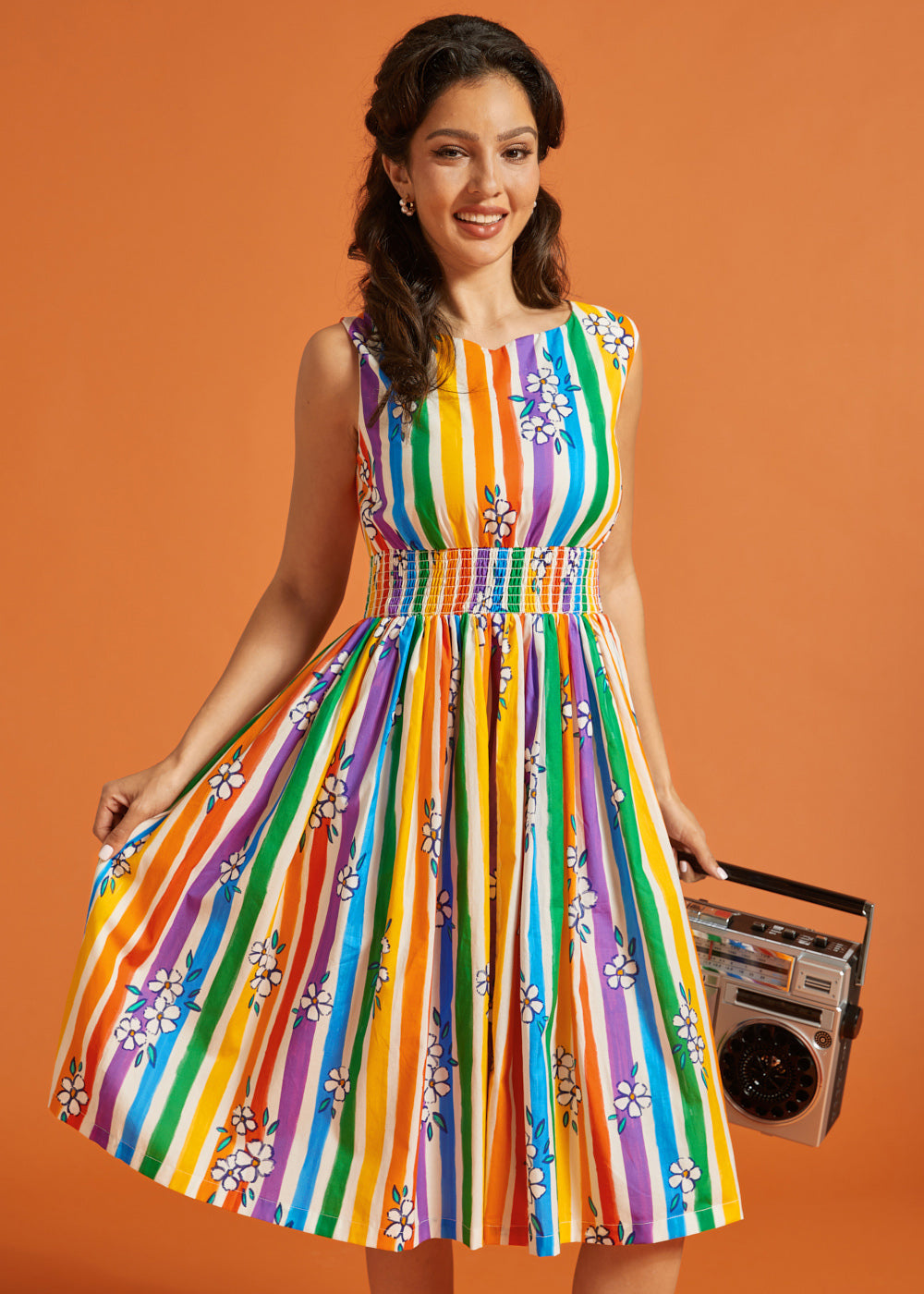 Woman wearing a colorful striped dress holding a boombox against an orange background