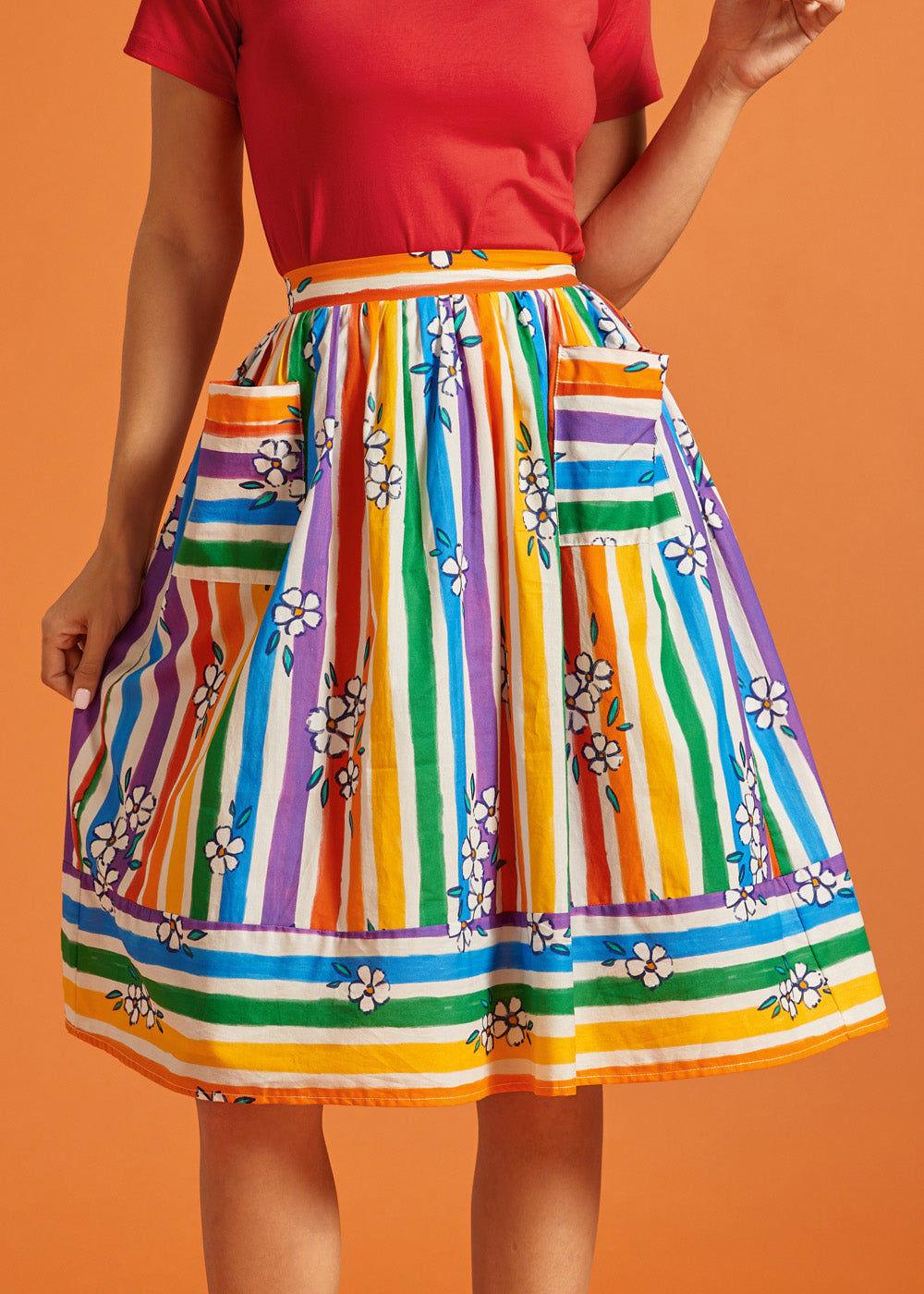 Woman wearing a colorful striped rainbow midi skirt with a red top on an orange background