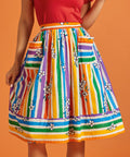 Woman wearing a colorful striped rainbow midi skirt with a red top on an orange background