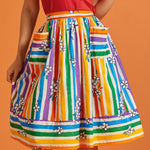Woman wearing a colorful striped rainbow midi skirt with a red top on an orange background