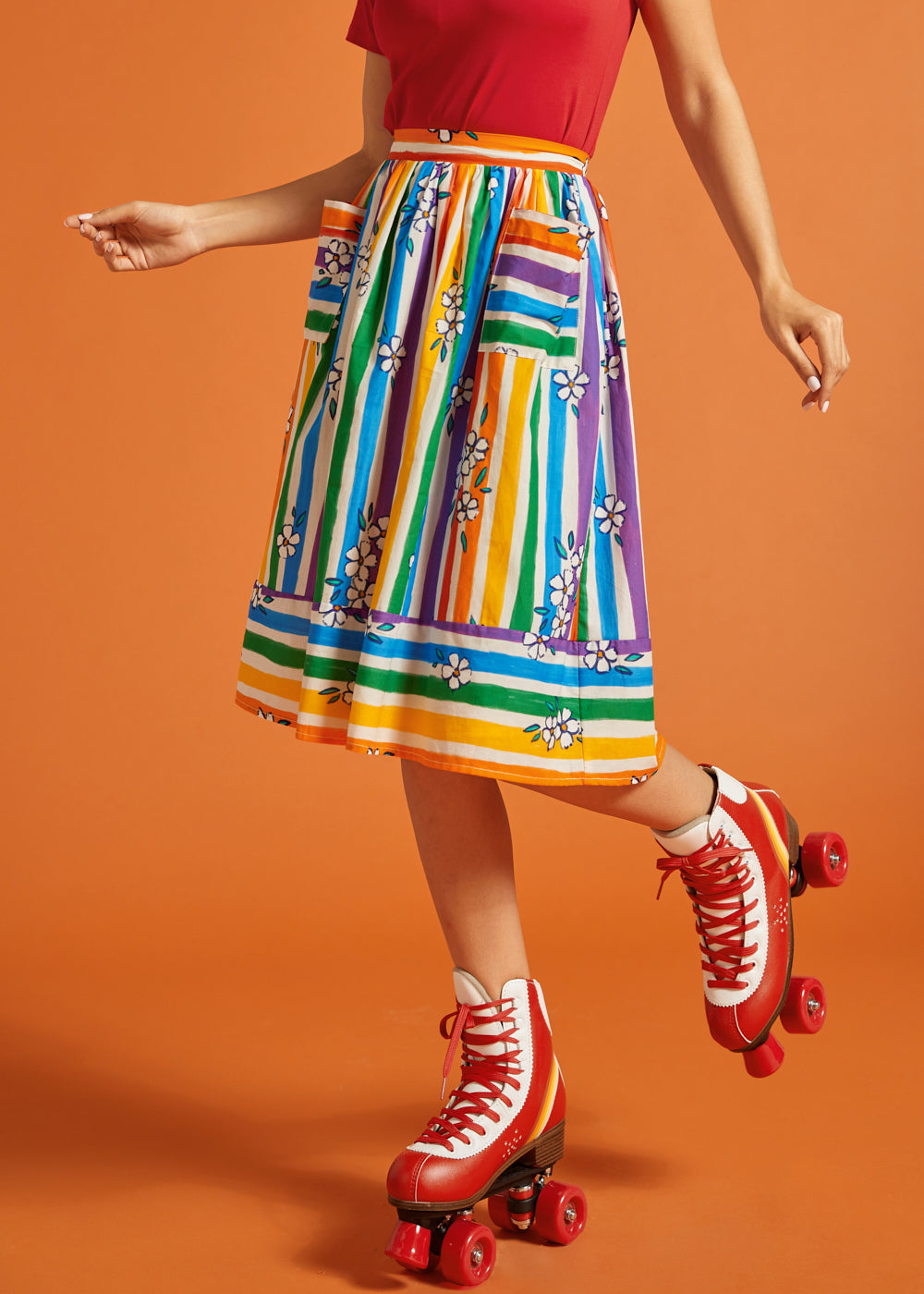Woman wearing a colorful striped skirt and red roller skates on an orange background