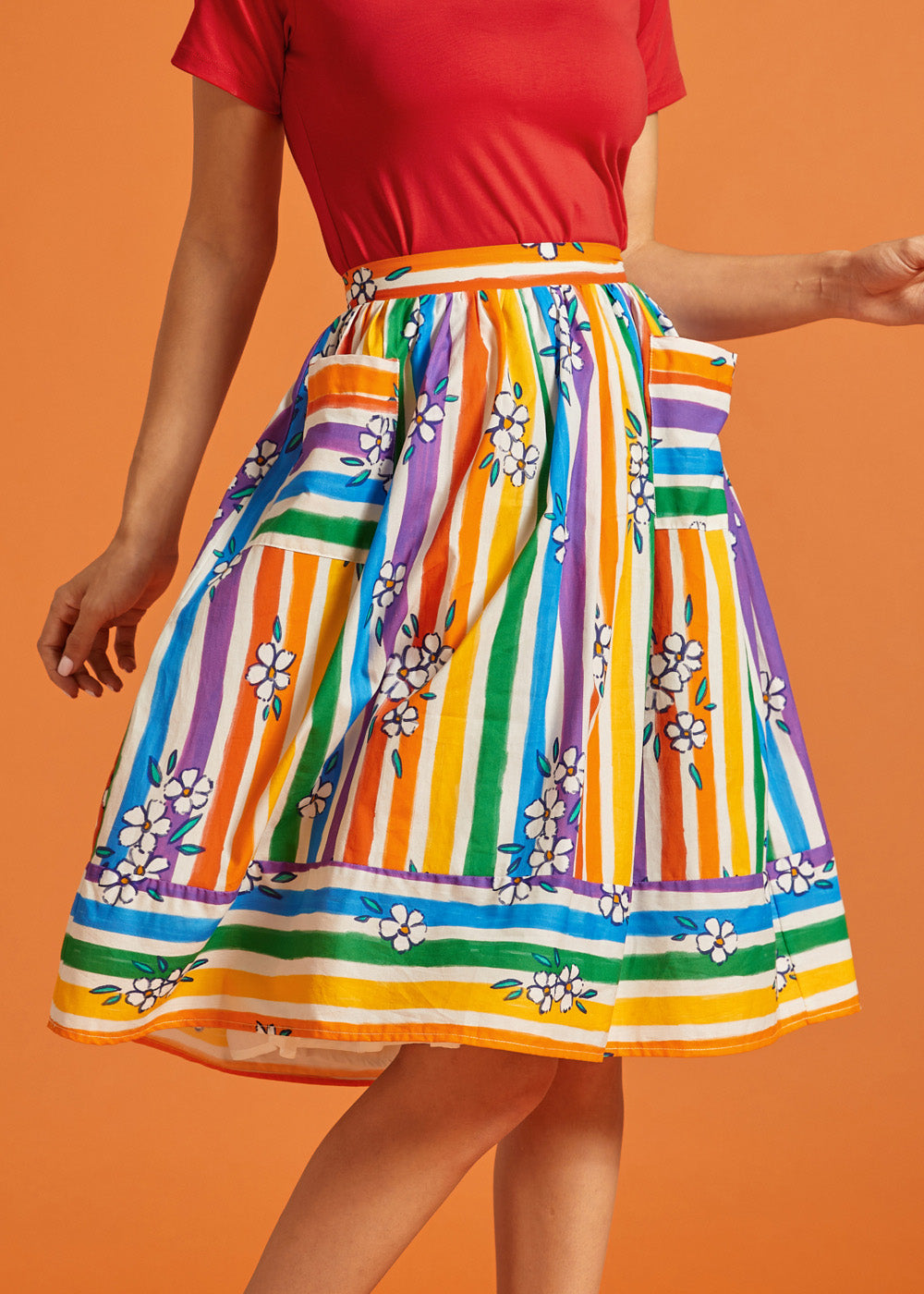 Woman wearing a rainbow stripe skirt with floral patterns, pockets, and a matching red top