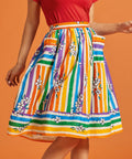 Woman wearing a rainbow stripe skirt with floral patterns, pockets, and a matching red top