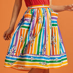 Woman wearing a rainbow stripe skirt with floral patterns, pockets, and a matching red top
