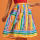 Woman wearing a rainbow stripe skirt with floral patterns, pockets, and a matching red top