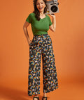 Woman holding a retro boombox, wearing a green shirt and rainbow patterned palazzo pants