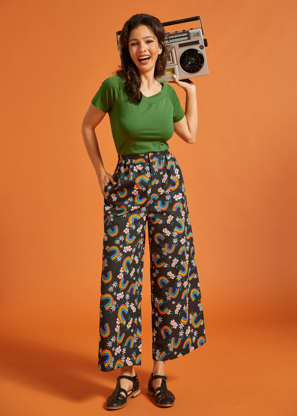 Woman holding a retro boombox, wearing a green shirt and rainbow patterned palazzo pants