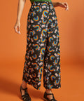 Woman wearing black pants with rainbow and floral pattern on an orange background