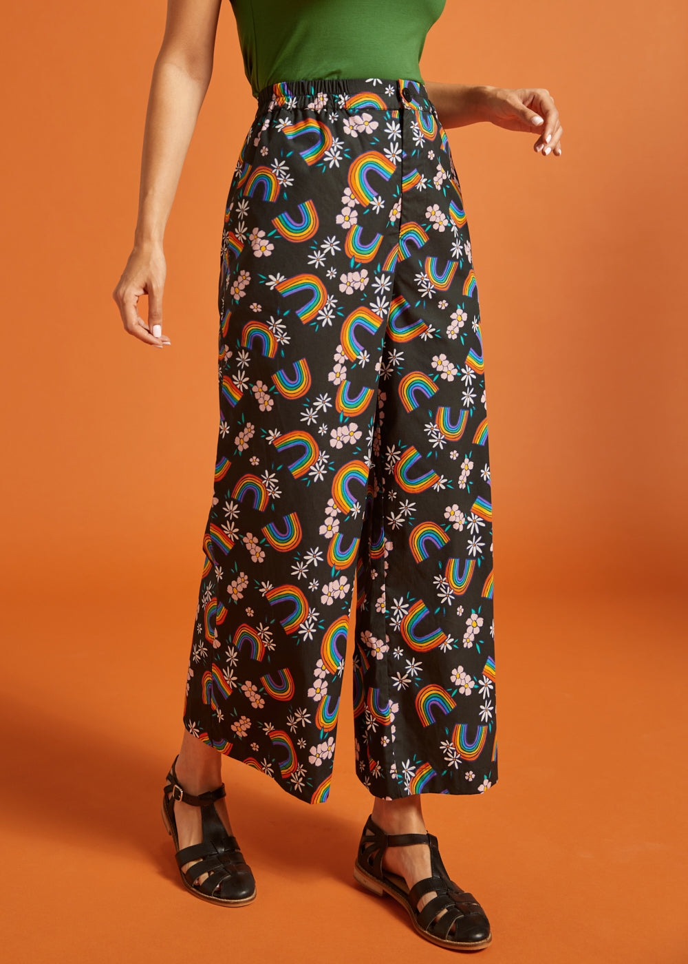 Woman wearing black pants with rainbow and floral pattern on an orange background
