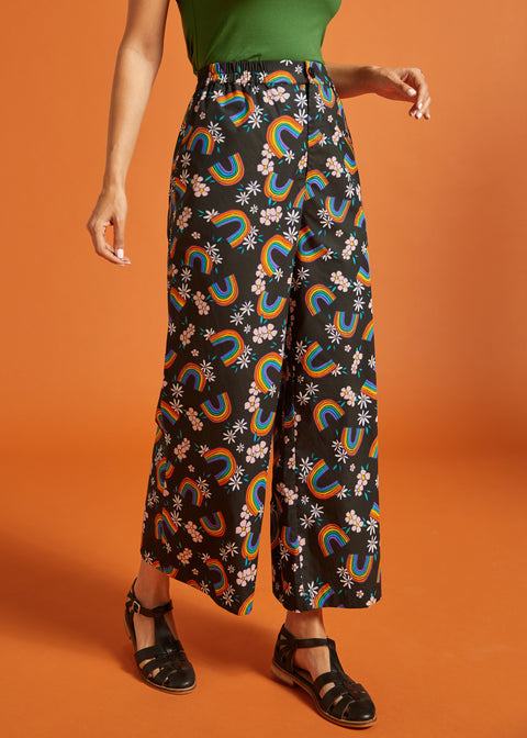 Woman wearing black pants with rainbow and floral pattern on an orange background