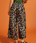 Back view of a woman wearing black wide-leg pants with rainbow and floral patternbackground