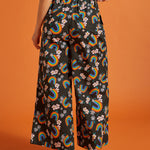 Back view of a woman wearing black wide-leg pants with rainbow and floral patternbackground