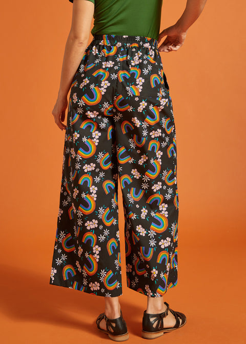 Back view of a woman wearing black wide-leg pants with rainbow and floral patternbackground