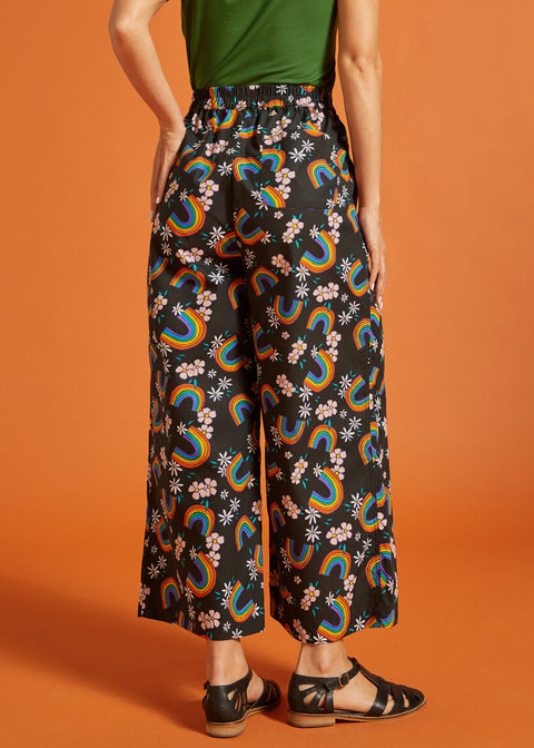 Back view of a woman wearing black wide-leg pants with colorful rainbow and floral pattern