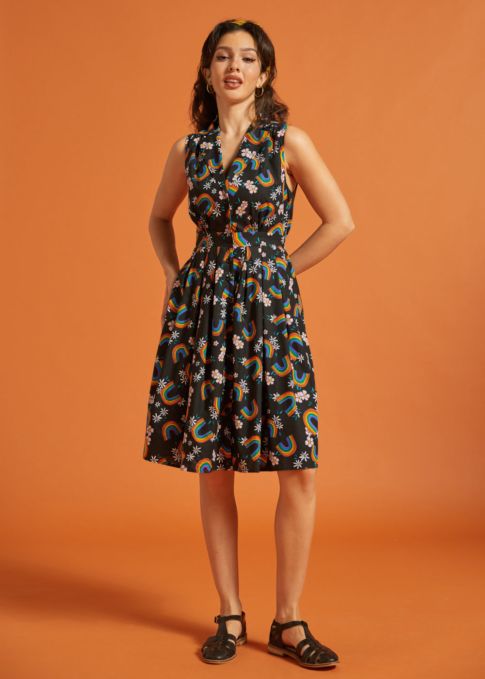 Woman wearing a sleeveless dress with a colorful rainbow floral pattern on an orange background