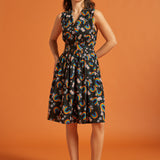 Woman wearing a sleeveless dress with a colorful rainbow floral pattern on an orange background