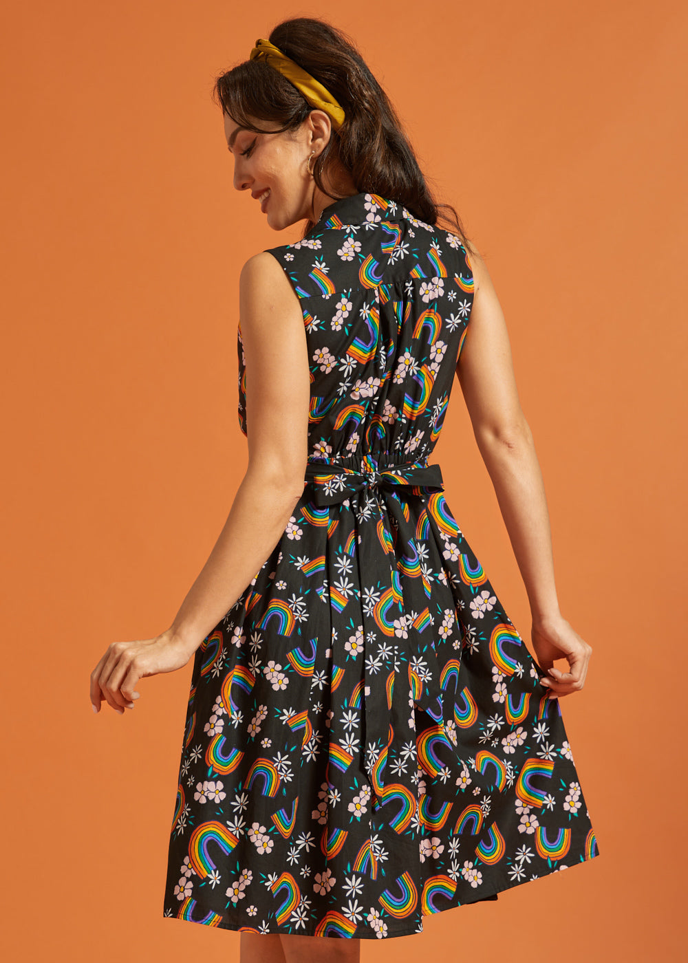 Back view of a woman wearing a dress with rainbow and floral pattern on an orange background