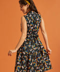 Back view of a woman wearing a dress with rainbow and floral pattern on an orange background
