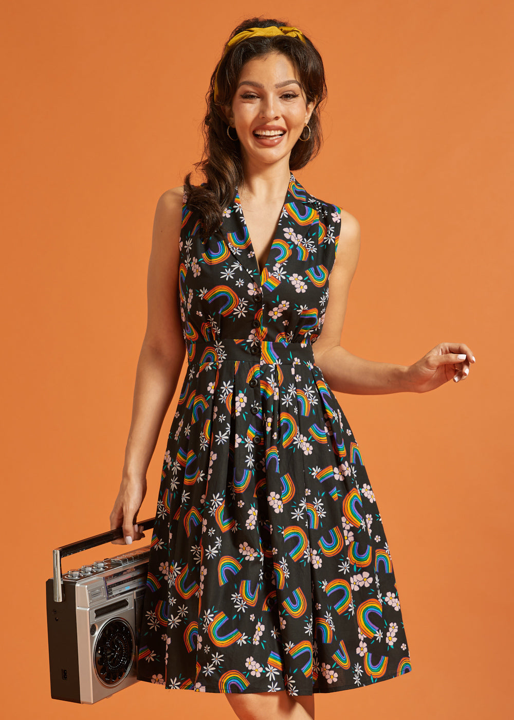 Woman wearing a sleeveless dress with rainbow pattern, holding a retro boombox