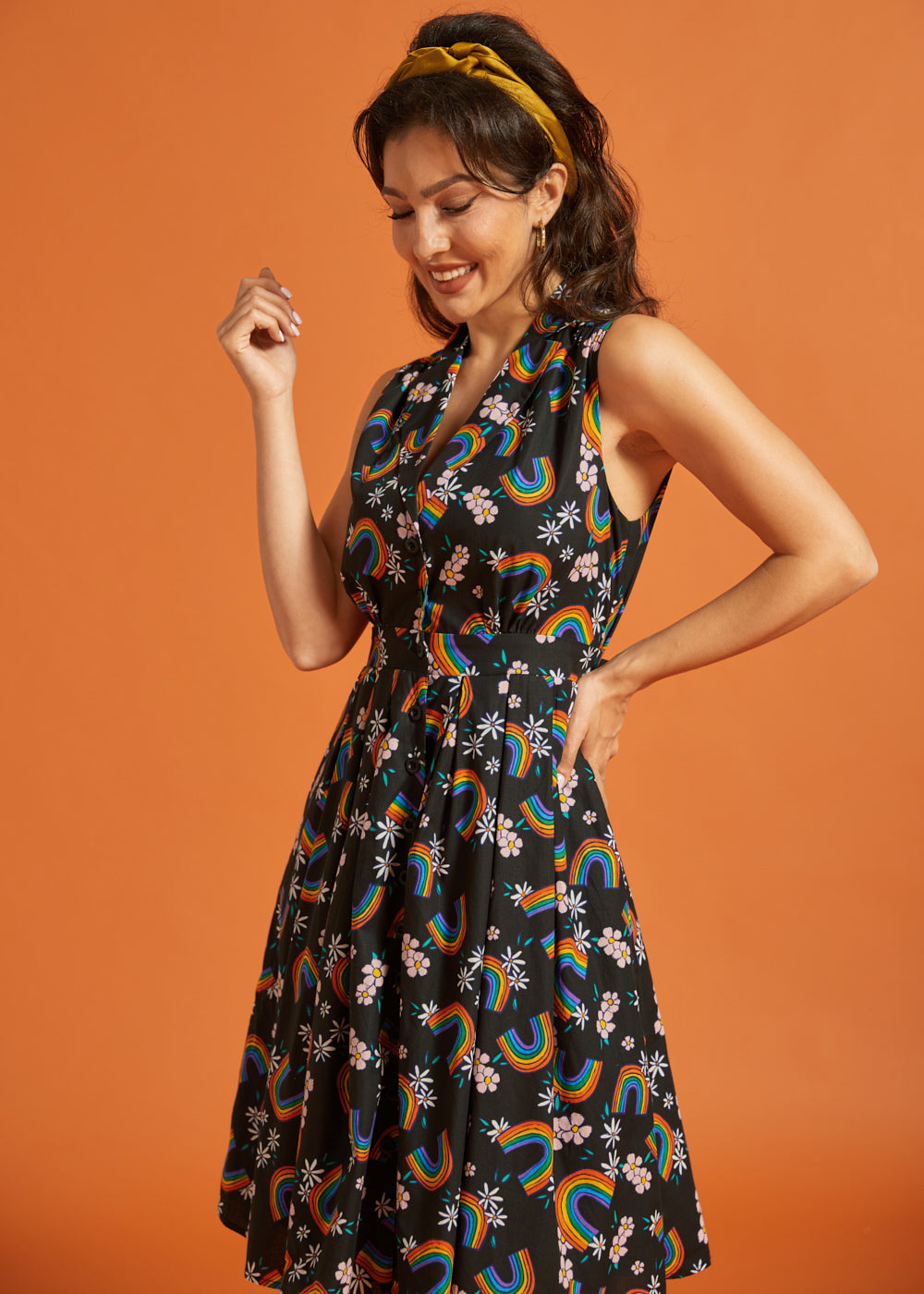 Side view of a woman wearing a black dress with colorful rainbow and floral pattern on an orange background