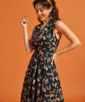 Side view of a woman wearing a black dress with colorful rainbow and floral pattern on an orange background
