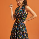 Side view of a woman wearing a black dress with colorful rainbow and floral pattern on an orange background