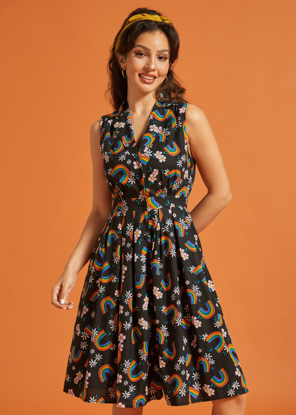 Woman wearing a sleeveless cotton summer dress with rainbow and floral pattern on an orange background