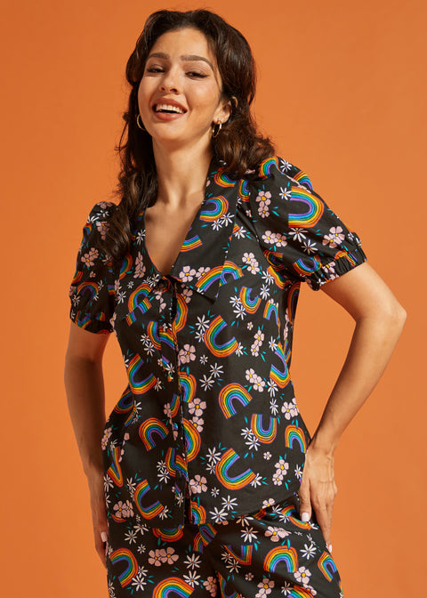 Woman wearing a button front summer blouse with rainbow and floral patterns