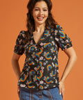 Woman wearing a black blouse with colorful rainbow and floral patterns on an orange background