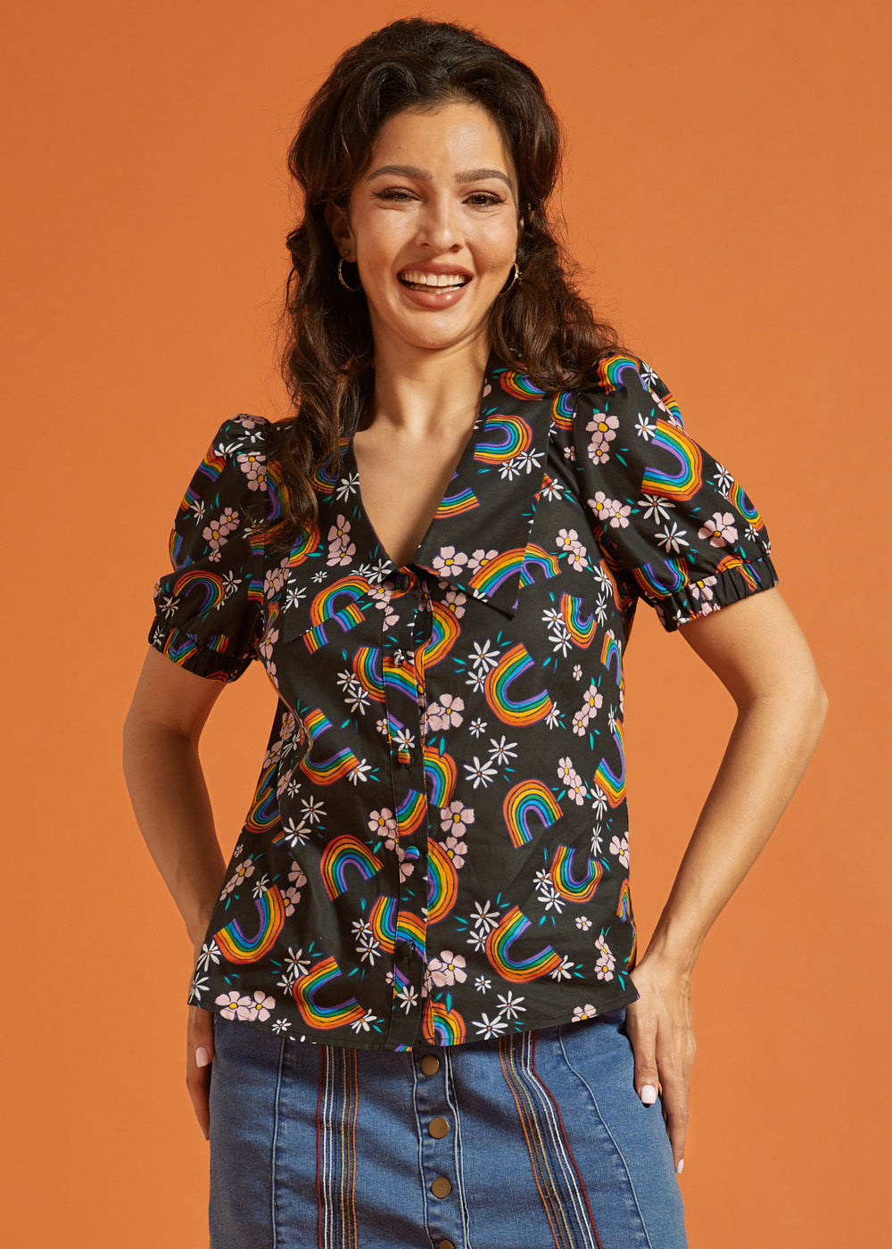 Woman wearing a black blouse with colorful rainbow and floral patterns on an orange background