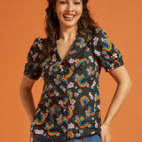 Woman wearing a black blouse with colorful rainbow and floral patterns on an orange background