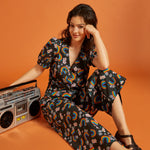 Woman in a floral rainbow print outfit sitting down with a retro boombox.