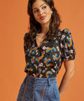 Woman wearing a black blouse with rainbow and floral patterns paired with a jean skirt