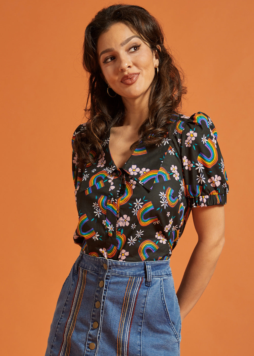 Woman wearing a black blouse with rainbow and floral patterns paired with a jean skirt