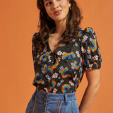 Woman wearing a black blouse with rainbow and floral patterns paired with a jean skirt