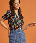 Woman wearing a vintage inspired colorful patterned top and blue jean skirt against an orange background